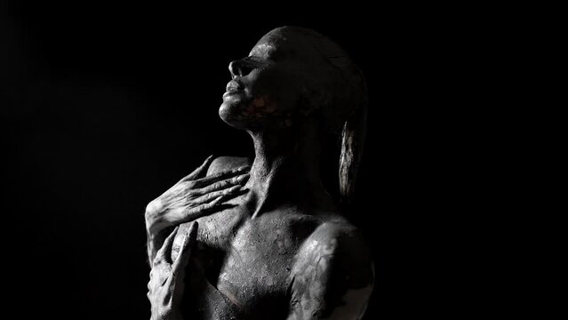 sensual blindfolded woman is smearing clay on her face and body, moving sexually in darkness
