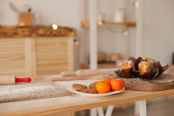 Wooden kitchen table covered with flour and with some fruit on it - baking in the kitchen and snacking with tangrines and cupcakes