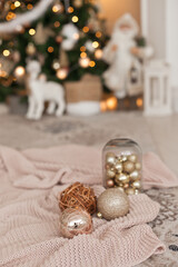 Gold shiny ornaments for christmas tree decoration on the pink knitted blanket. Festive holiday decorating in the living room. 