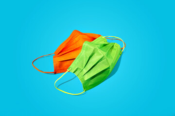 Minimalist medical still life of green and orange respiratory or surgical face mask on blue background. Bright and trendy coronavirus or dust protection supplies. Pandemic concept. Disposable mask.