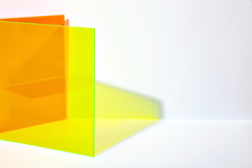 Saturated orange and neon yellow acrylic sheet with long shadow on a bright lit white background. Stylish abstract background. Stage for advertising, promoting new products.
