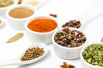 Various spices for cooking, laid out in white bowls and spoons, close-up.