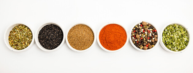 Types of spices of different colors scattered in ceramic bowls isolated on white background