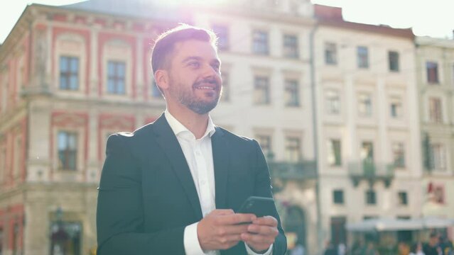 Close up front view cinematic portrait of young handsome caucasian man walking and scrolling phone. Camera 360 shot. Man in smartsuit. Sunlight glare.