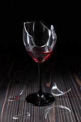 A broken wine glass with remnants of red wine on a wooden table. Selective focus.