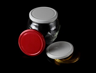 Empty new glass jar and colorful lids isolated on black  