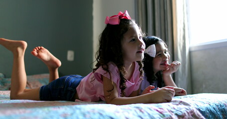 Two little girls watching TV screen in bed laughing and smiling
