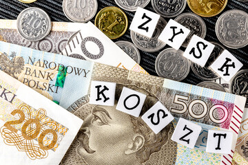 The wording "zysk koszt" translated as "profit cost" and many Polish coins and banknotes on the black background. New taxation rules in Poland.