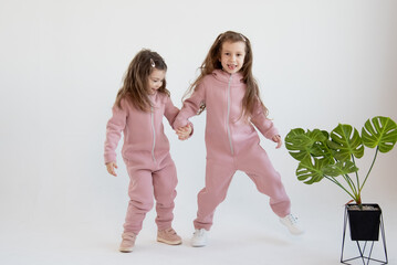 Two cute little girls in a pink overalls sits stand together. White background. Fashion. Childhood.