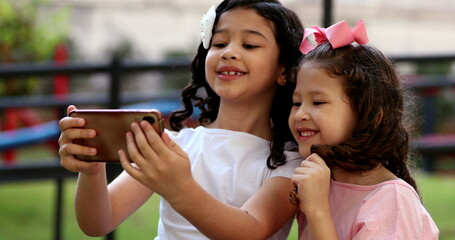 Obraz premium Two little girls posing for selfie with smartphone, children take photo with front camera