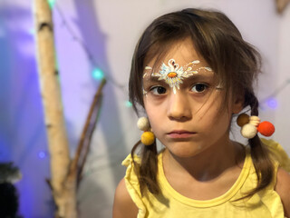 a serious little girl with disheveled pigtails stares intently and her face is decorated with a pattern of swans and a daisy