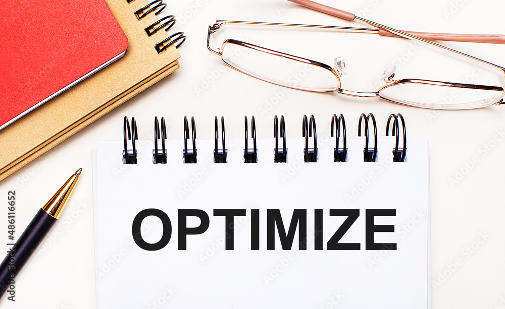 Poster on a light background - glasses in gold frames, a pen, brown and red notepads and a white notebook w