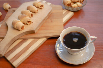 Croissants with apple jam and a cup of coffee on a wooden background.