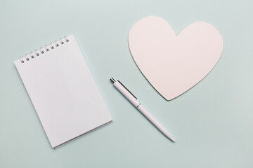 Top view of open spiral blank notebook with pen and white paper heart on white desk background. Isolated on mint color backdrop. © Oksana Boeva