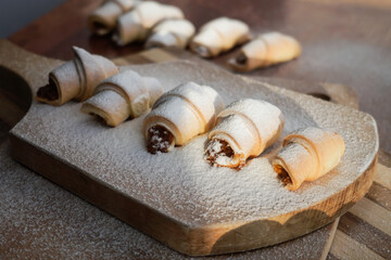 Croissants with apple jam sprinkled with powdered sugar on a wooden background.