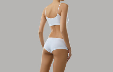 Obraz premium Crop rear view of toned sexy female model in underwear isolated on grey studio background. Slim woman back butts in organic cotton underclothing wear or pajama advertise good quality home garment.
