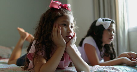 Two little girls laid in bed watching television. kids in front of TV