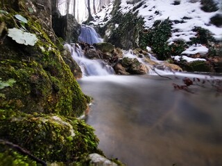 Beautiful mountain stream between rocks  with small waterfall on a snowy winter day