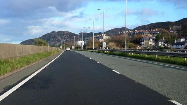 2 clips, unreadable car brand logos and number plates. Car front view driving highway A55 called North Wales Expressway in a beautiful Welsh mountain scenery in autumn.