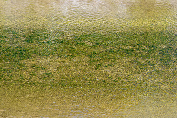 Surface of the water with ripples, through which a sandy bottom with small pebbles shines through, for use as an abstract background and textures.