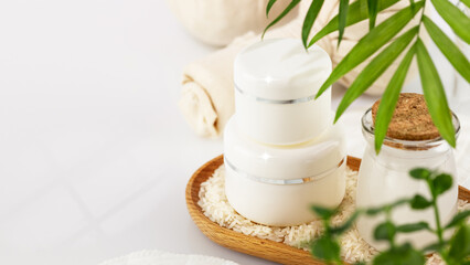 Fermented beauty care. Wellness composition with hande made rice water, creams and rice grain on a wooden plate on a white table with copy space. Natural homemade cosmetics based on fermented product