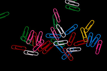Colored paper clips isolated on black background.