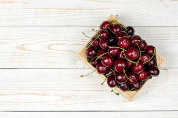 Cherries in box. Sweet fresh cherries in wooden box on white background. Plat lay, top view.