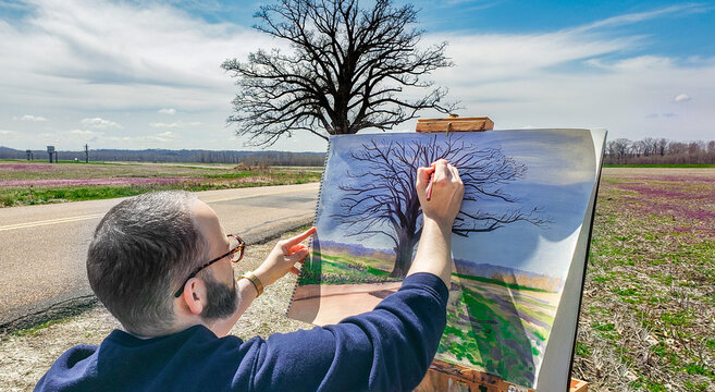 View of man drawing landscape scene with old oak tree early in spring, sky in background