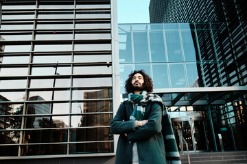 Man looking away while posing with his arms crossed against an office building at the financial district.