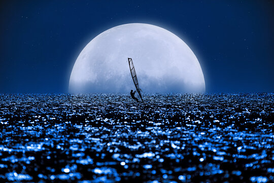 Windsurfer surfing on moonlit ocean waters.