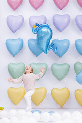a cute little girl with balloon in the form of a flamingo in hands having fun on colorful heart balloons background. smiles,funny Valentine s Day birthday party