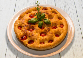 Apulian focaccia, typical italian Bari pizza made with a dough of durum wheat flour and potatoes  with cherry tomatoes on top. In white plate on white wooden table