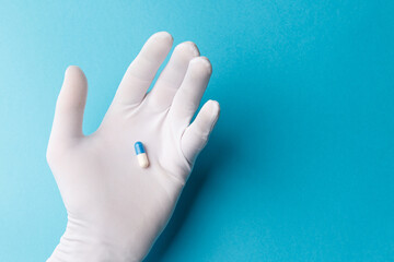 The concept of a cure for all diseases. A white-gloved hand holds a blue-and-white pill with...