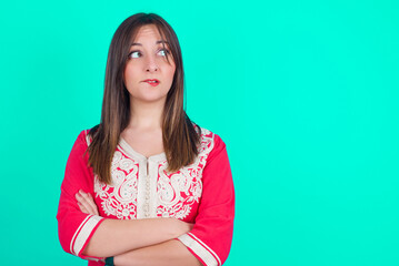 Amazed young beautiful moroccan woman wearing traditional caftan dress over green background...