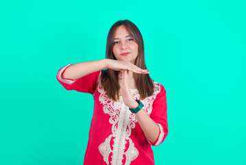 young beautiful moroccan woman wearing traditional caftan dress over green wall being upset showing a timeout gesture, needs stop, asks time for rest after hard work, demonstrates break hand sign