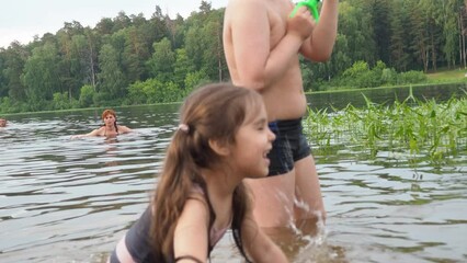 happy children, boy and girl swim in a forest lake. splashing each other. play. enjoying vacations and outdoor recreation. in blue water at sunset; bathe in lake or river and making water drops