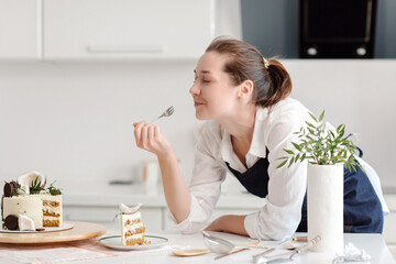 Obraz na płótnie Canvas A woman confectioner in a blue apron is eating a piece of chocolate cake. Tasting delicious chocolate cake. High quality photo