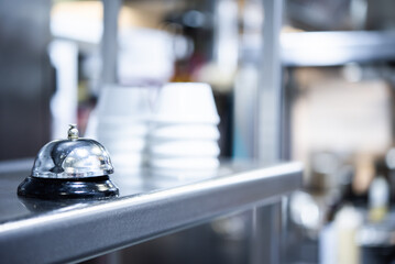 Hand bell to call the waiter and in the background a chef working in a professional restaurant kitchen prior to service. chef at work