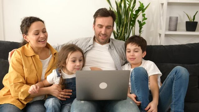 Family of four using laptop for video connection with grandparents or family. Multiracial mom, dad and two kids waving in webcam of the laptop, video call, virtual meeting concept