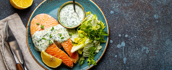 Healthy food meal cooked grilled salmon steaks with white dill sauce and salad leafs on plate on rustic concrete stone background table flat lay from above, diet healthy nutrition dinner