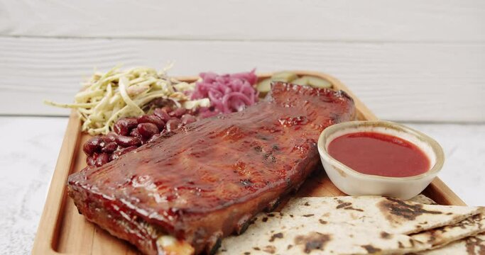 A large Plate that includes Baby Back Ribs with cherry chipotle sauce. cooked slowly on smoker, sauce, BBQ beans, coleslaw, pickled onions, pickled cucumbers, Rotating on isolated white background