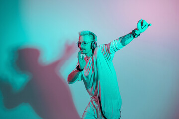Hipster man listen to music and dances on a colorful pink and blue background. Fashion guy with headphones moving in the rhythm of dance in studio