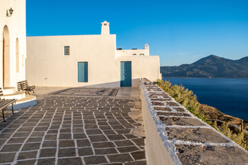 Greece, Milos island, Chora town, Plaka. White building and stone paved yard over calm sea, Cyclades