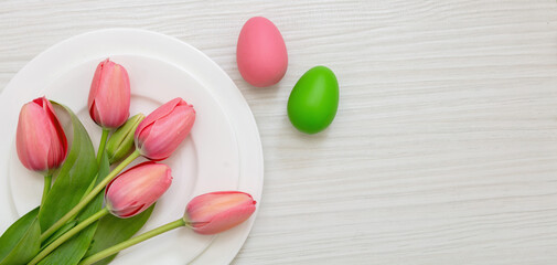 Easter table decoration. Egg pastel color in a plate and pink tulip on white wood, overhead