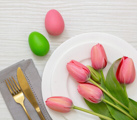 Easter table setting. Egg pastel color and pink tulip and gold cutlery on white wood, overhead