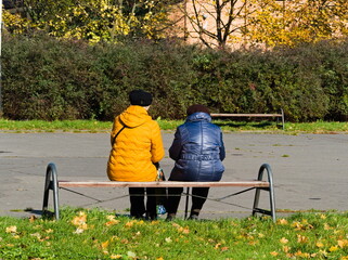 Two elderly people sitting on a bench. Retired people resting. Conversations on the bench. Two people wearing warm jackets