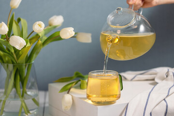 Pouring green tea into a glass cup and white flowers