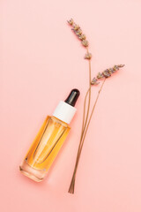 A transparent glass bottle with a pipette and dry lavender on a pink background. Vertical orientation, flat lay. The concept of organic care cosmetics and beauty products