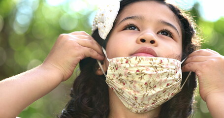 Child trying to put covid-19 face mask outside in nature