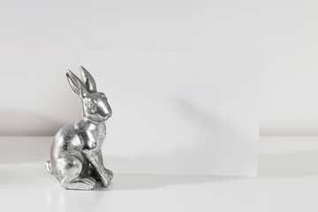 Mock up white frame with modern ceramic easter bunny decor on a shelf. White color scheme. Landscape frame orientation.